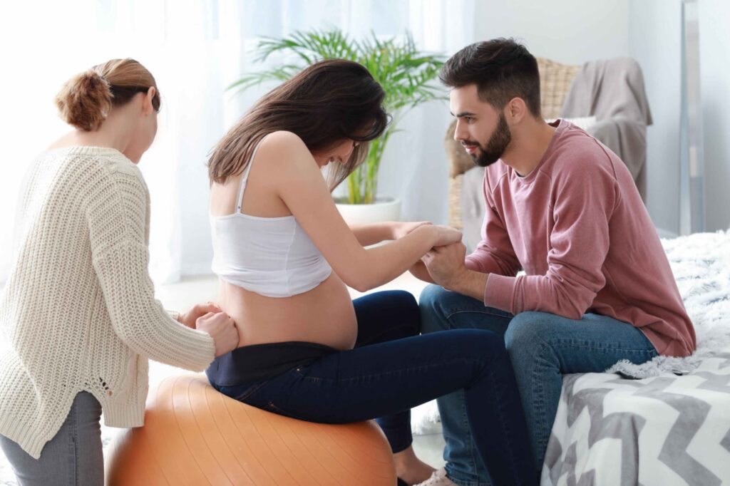 Doula giving counter pressure while pregnant woman is sitting on ball