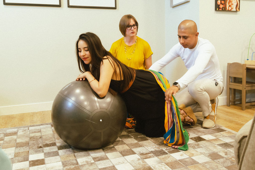 Pregnant woman leaning on birth ball while husband uses rebozo with doulas help