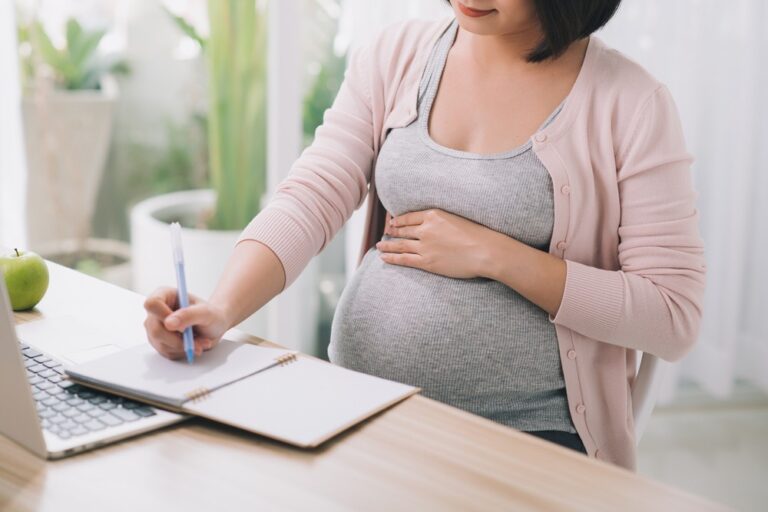 Pregnant woman writing birth plan at computer